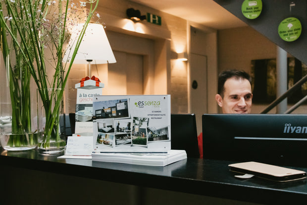 Person behind a reception desk with promotional materials and a plant in the foreground