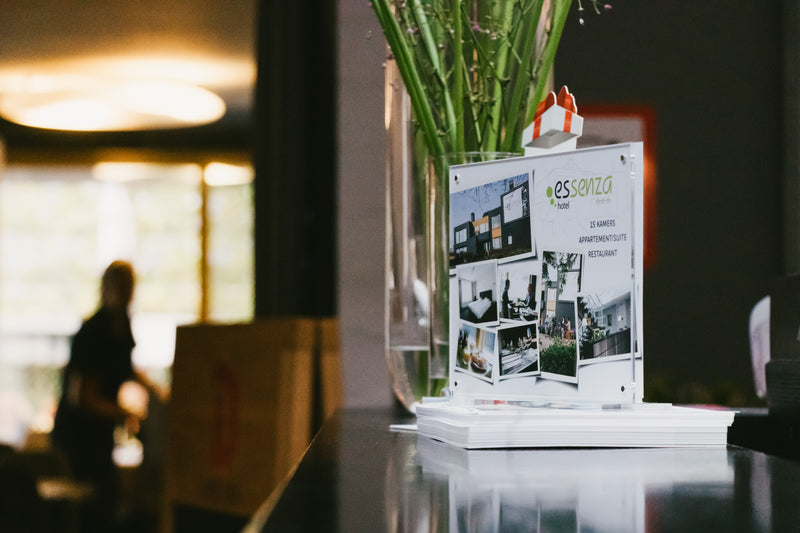 Vase with greenery and a small model building on a table with blurred background and a photo acrylic panel