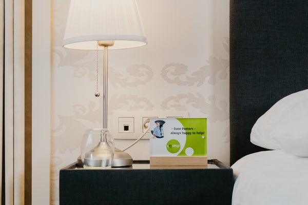 Lamp on a nightstand next to a bed with a branded acrylic bamboo panel