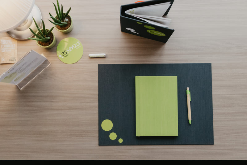 Green notebook and pen on a black mat with a wooden surface background
