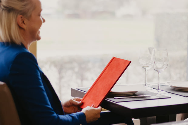 Persoon bekijkt een rode gepersonaliseerde menukaart aan tafel in een restaurant