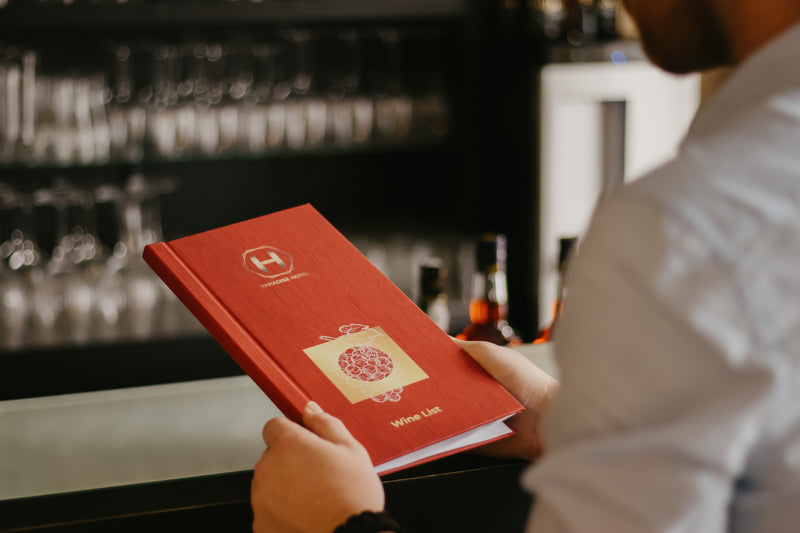 Person holding a red menu with a logo in a bar setting