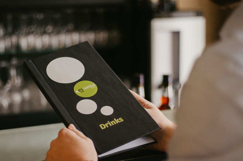 Person holding a menu with 'Drinks' section at a bar.