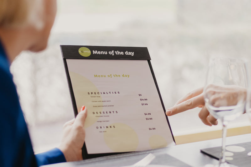 Person holding a clipboard menu with the specials of the day in a restaurant setting