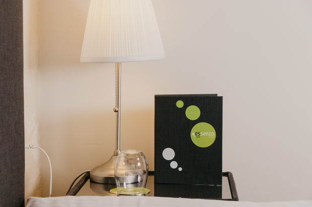 Lamp, glass, and black menu with green logo on a table against a beige wall.