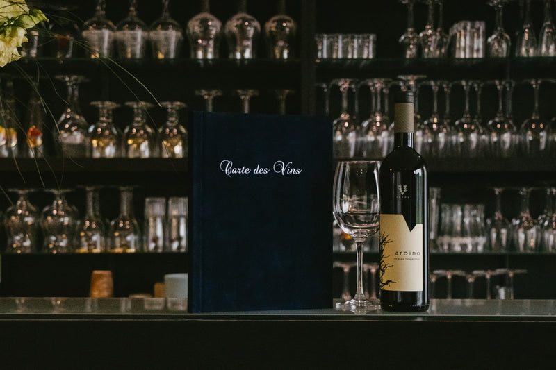 A black menu with white printing on the front in a bar with wine and a glass
